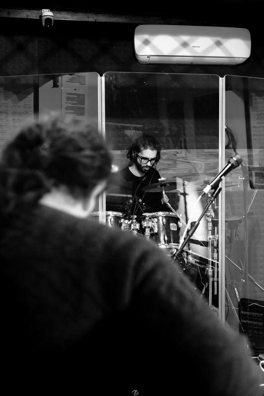 Drummer seen through the booth glass in a rehearsal room, black and white