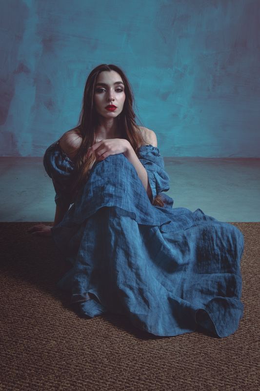 Editorial portrait: blue linen dress, seated on the floor against a teal wall