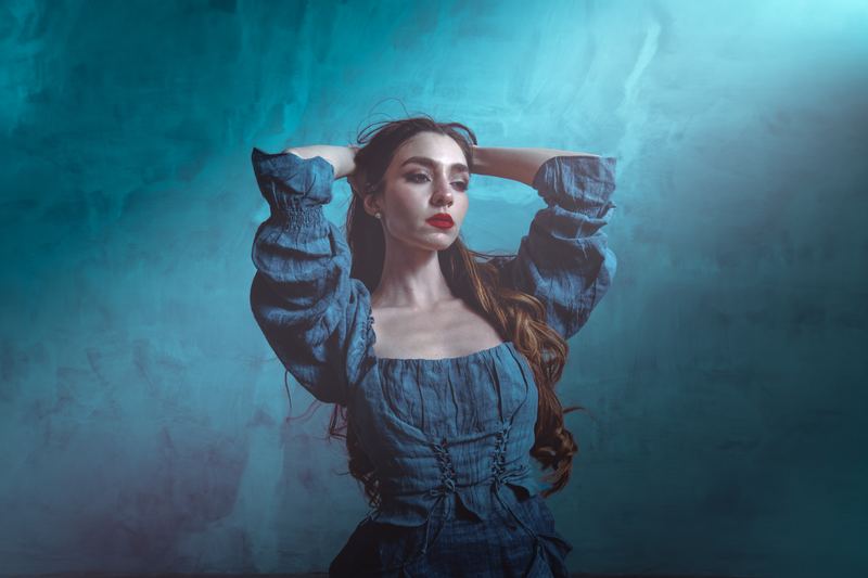 Fashion portrait: arms raised into the hair, denim against a teal backdrop