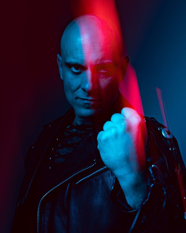 Studio portrait under split red and blue light, a closed fist in the foreground