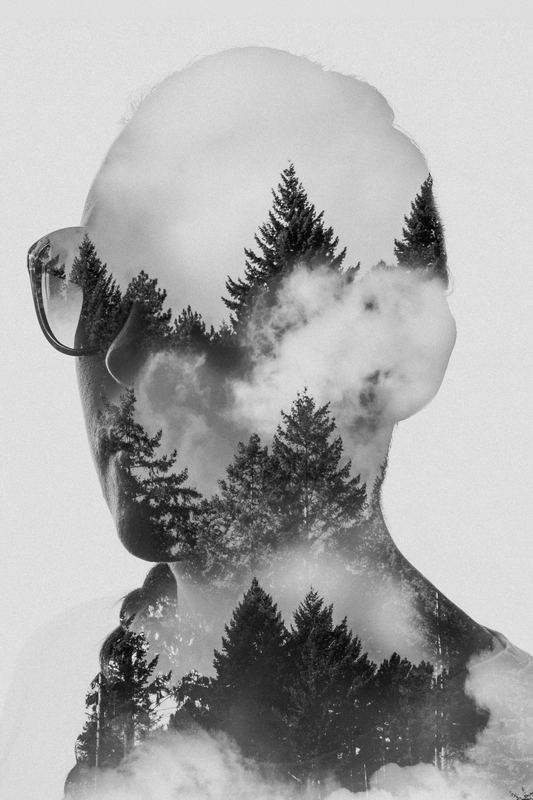 Black and white double exposure: a profile with glasses filled with pines and clouds