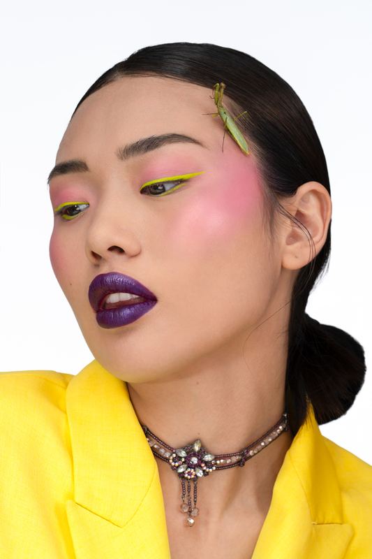 Beauty portrait in profile: purple lips, pink cheeks and a green mantis in the hair