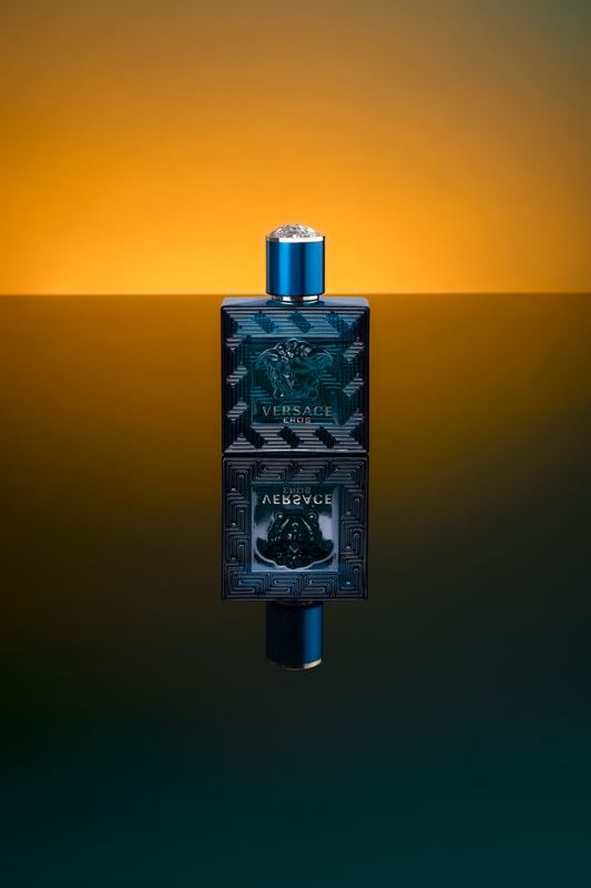 Dark perfume bottle mirrored on a glossy surface with orange and green light
